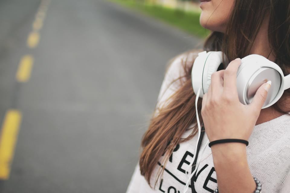 Woman holding white headphones while walking along a road