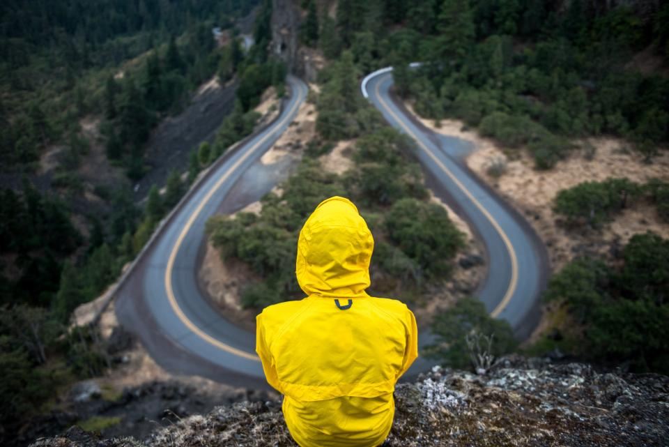 Person in a yellow rain jacket above a winding mountain road